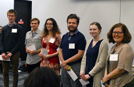 Mixed group of UIC students hold envelopes containing their Kade awards and Prof. Sara Hall