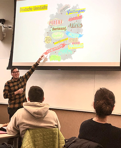 A male graduate student points to a map of Germany projected on a screen